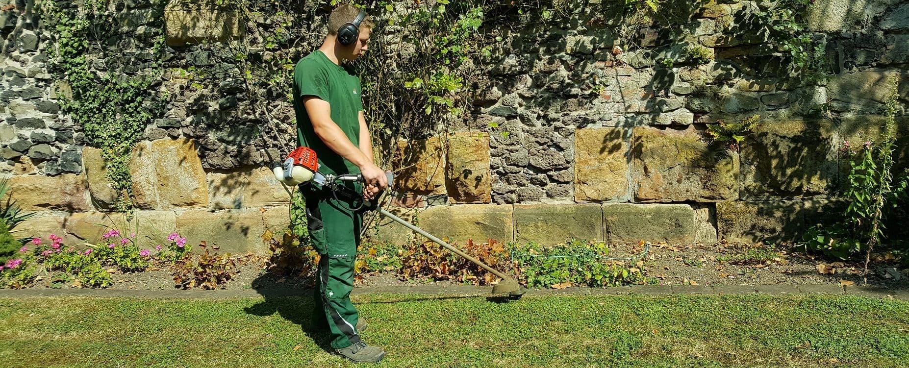 Mitarbeiter bei Pflegearbeiten entlang einer alten Natursteinmauer