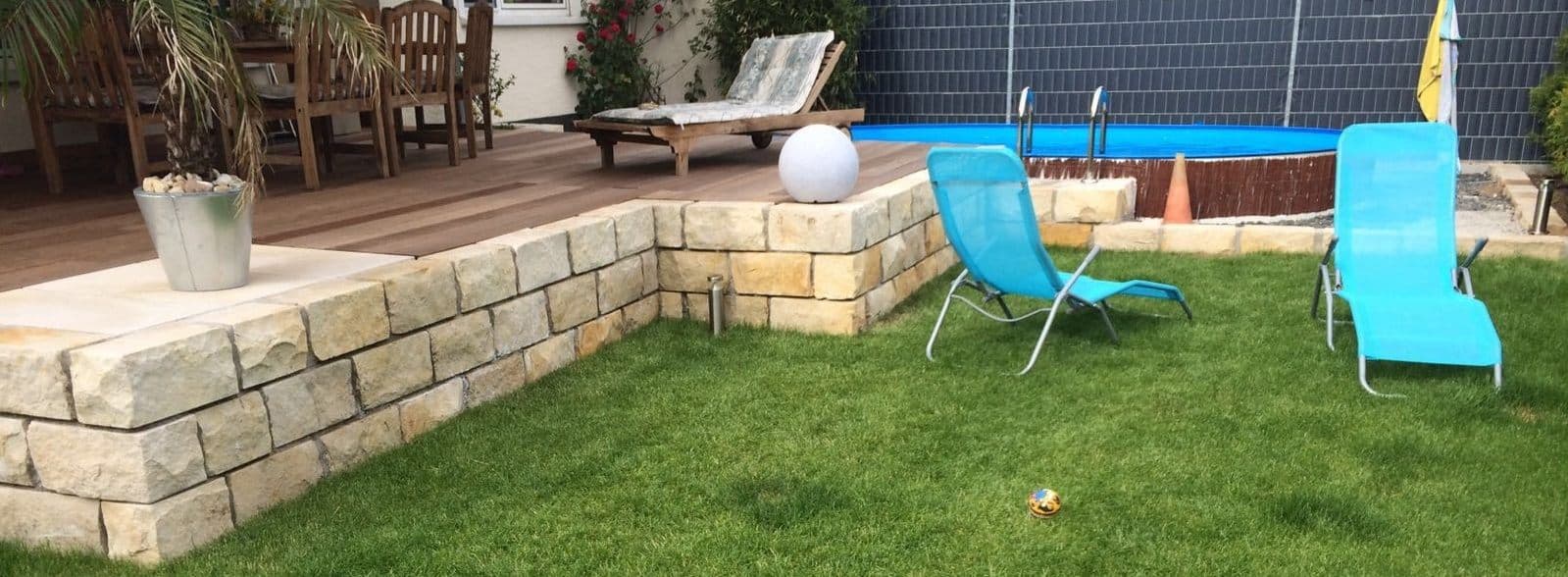 Natursteinmauer und Rasenfläche rund um einen Pool